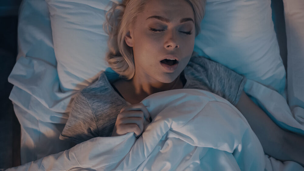 Žena hrče u krevetu — simptomi apneje u snu