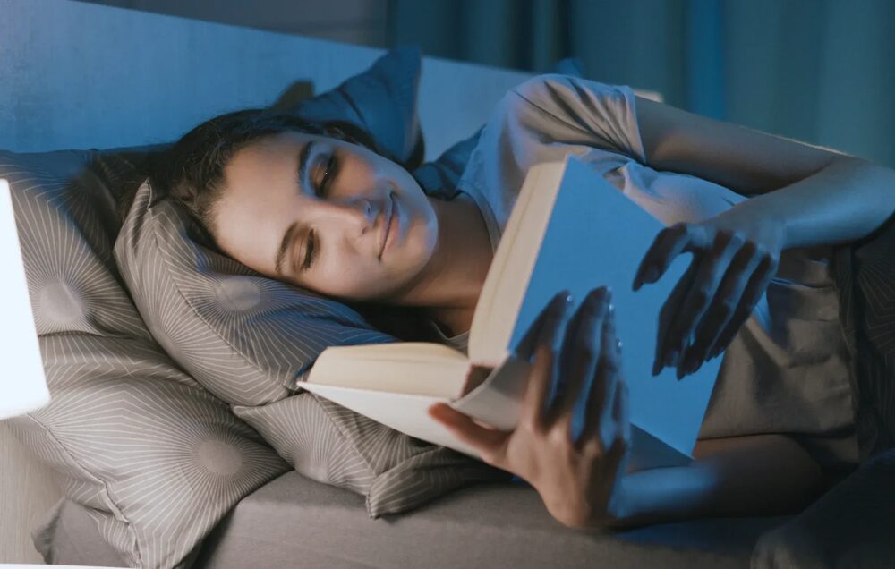 Žena čita knjigu u krevetu uz toplu lampu pred spavanje